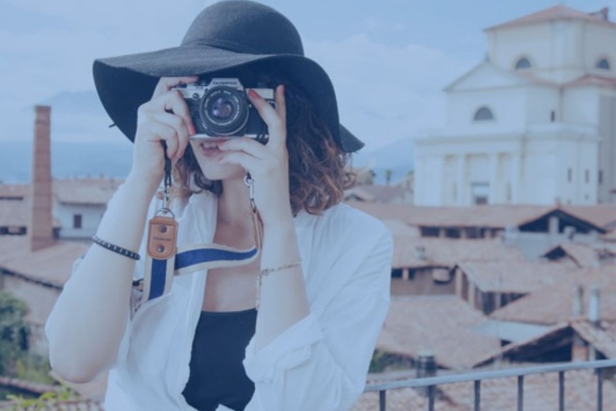 female photographer with floppy hat and houses behind her